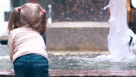 cu back view slow motion little sweet girl playing with water near fountain sprays water with a hand