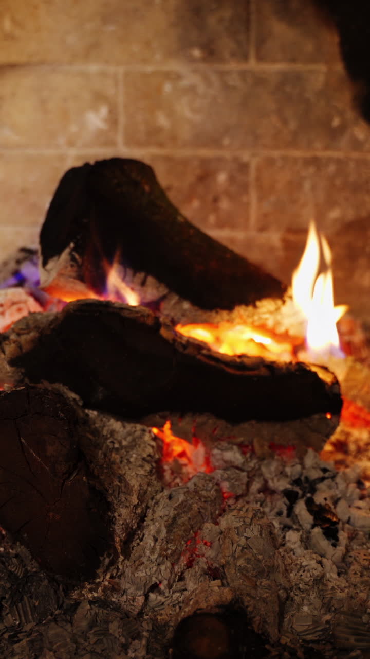 Cozy fireplace. Smoldering logs in ash. Embers of burnt-out fire in fireplace at home. Background of burning wood in slight flame. Close-up. Vertical video