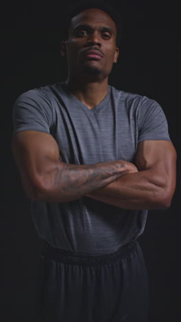 vertical video portrait of male boxer training putting up fists before folding arms against black background