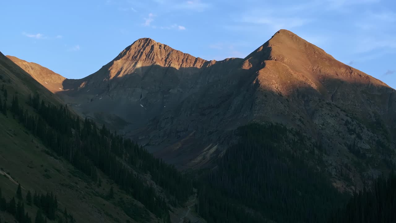Tampilan udara dekat dari puncak alpine yang terjal menangkap cahaya hangat matahari terbenam, alpenglow, bergerak ke kiri.