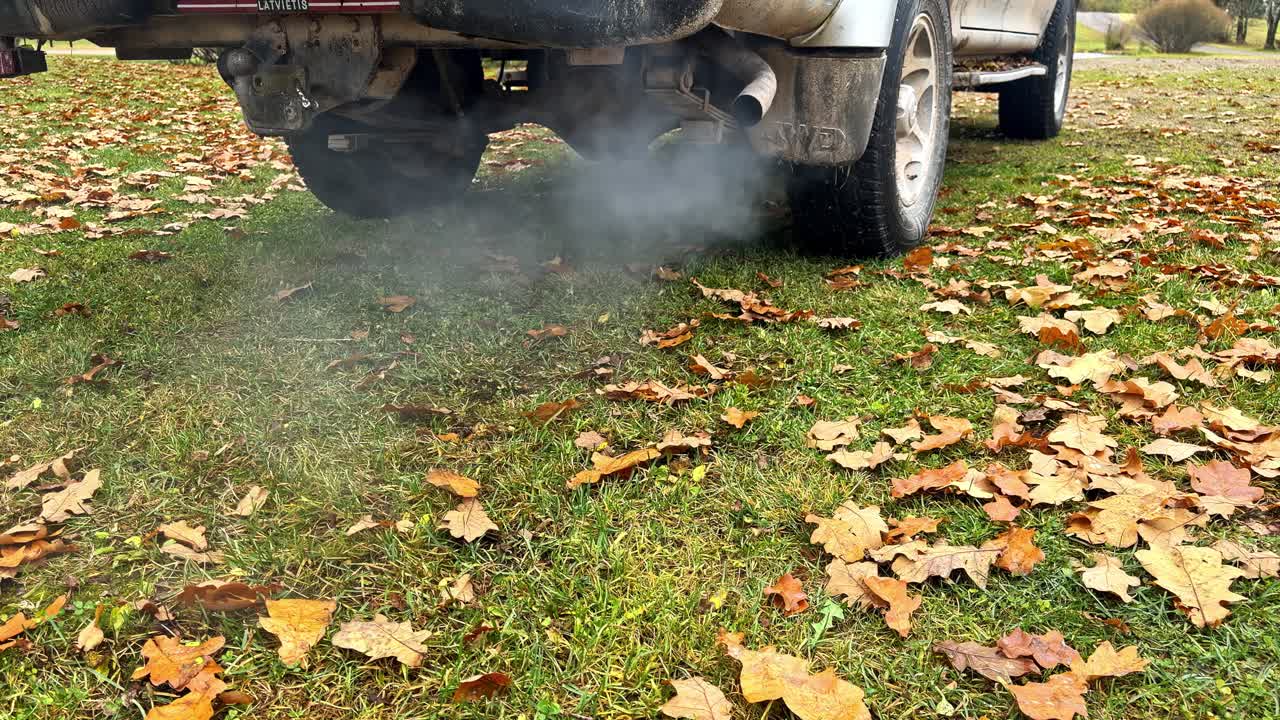 Exhaust smoke rising from off-road vehicle parked on grassy field with autumn leaves
