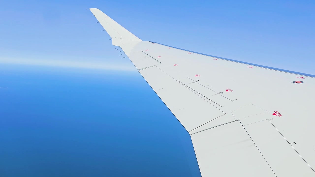 Utsikt over flyvinge over dypt blått hav og klar himmel fra passasjervinduet, flyet flyr i stor høyde over vannet, reise- og transportopptak, luftperspektiv og rolig naturskjønn flytur.