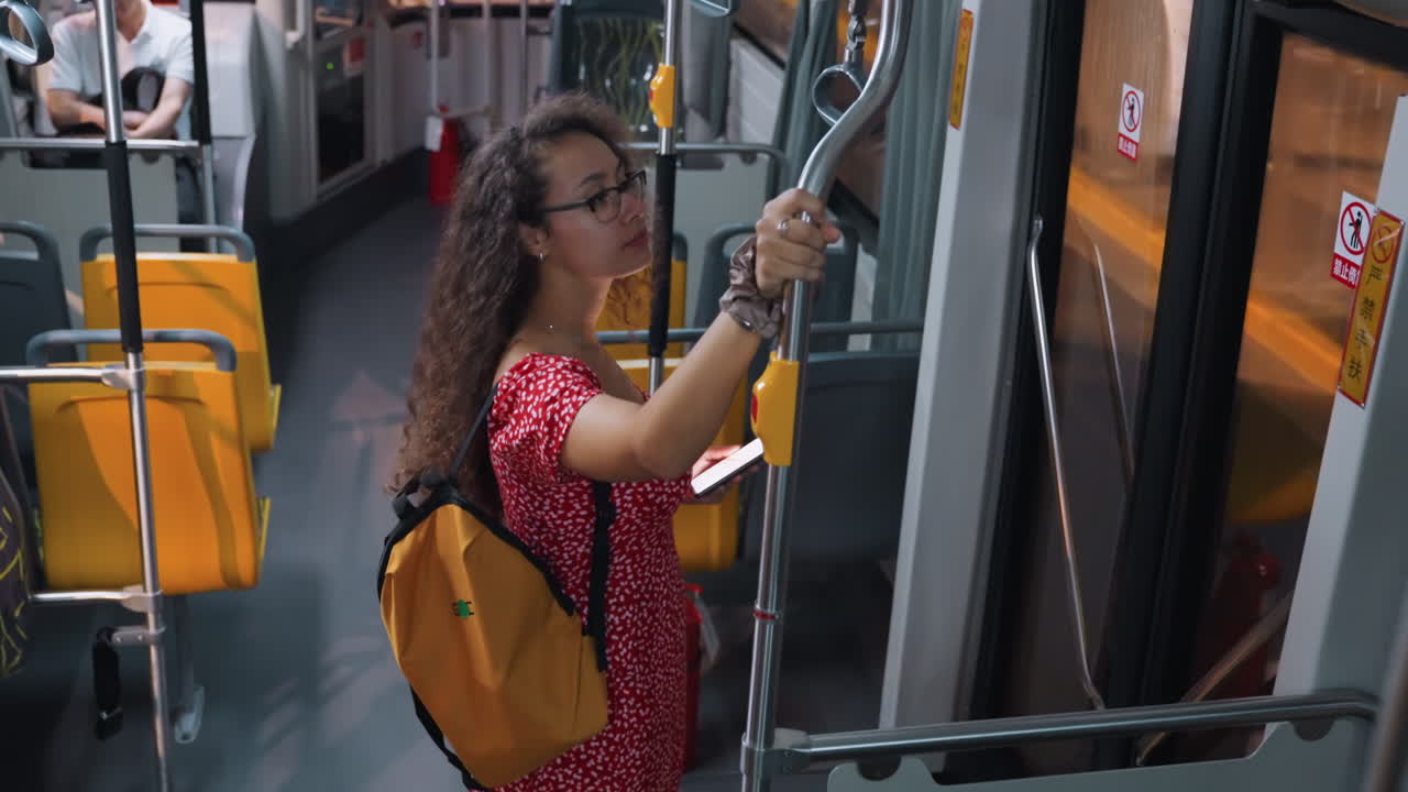 Donna con capelli ricci che sale sull'autobus, che afferra il corrimano e indossa uno zaino giallo, un vestito rosso, tranquillo tragitto serale urbano, ritratto urbano spontaneo che cattura il movimento e il riflesso del finestrino, interni moderni.