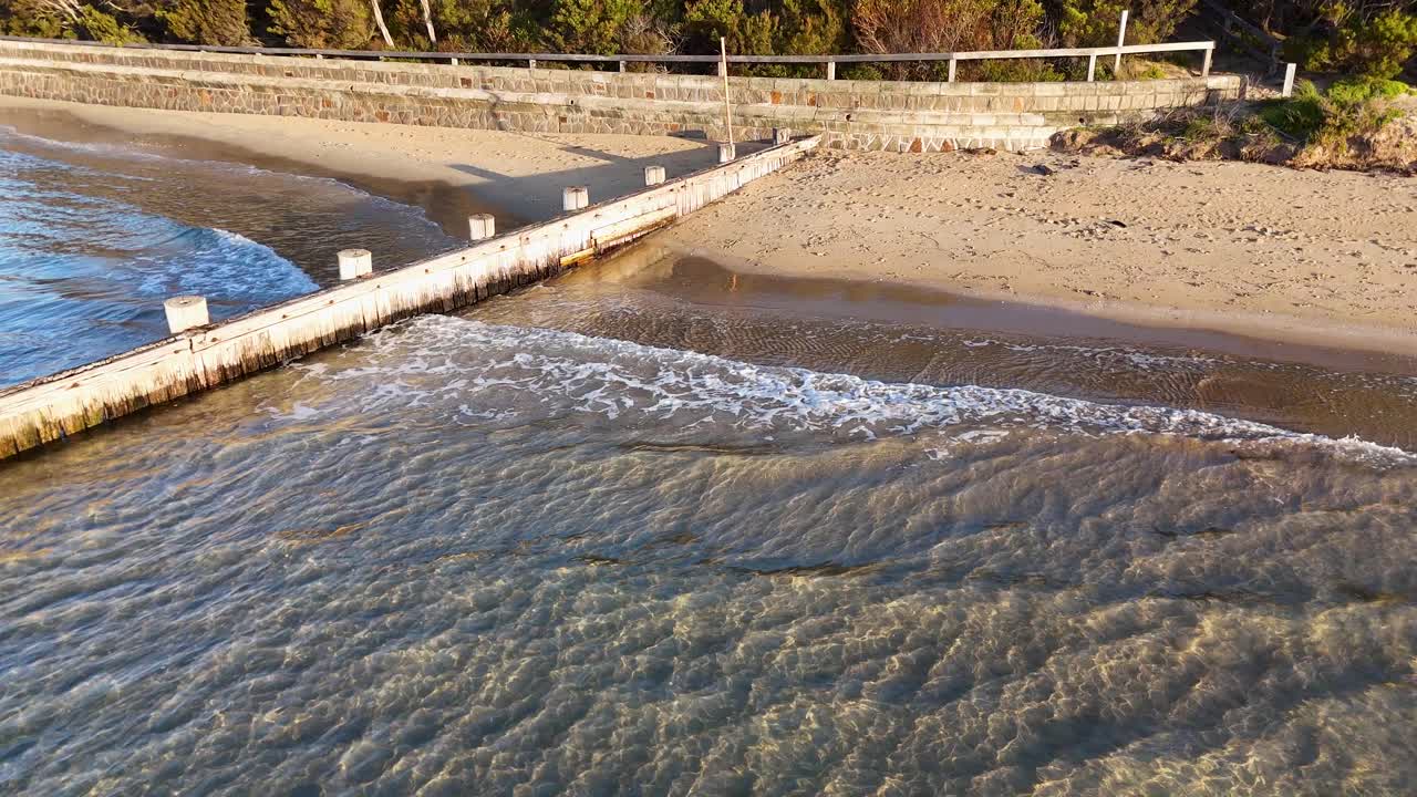 Onde che interagiscono con una diga frangiflutti in legno su una spiaggia sabbiosa, a dimostrazione delle strutture di protezione costiera