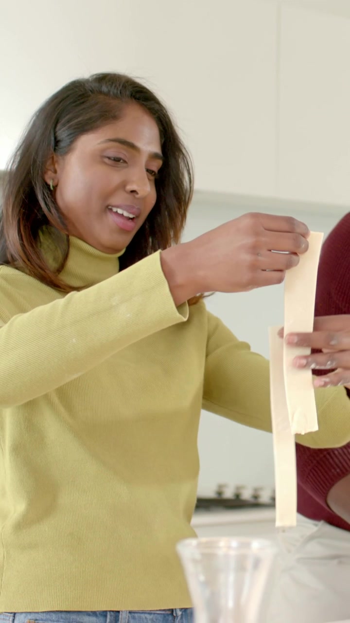Video verticale: Donna con top color menta che prepara la pasta su un tagliere ai fornelli, uomo in rosso che aiuta, spazio per il testo.