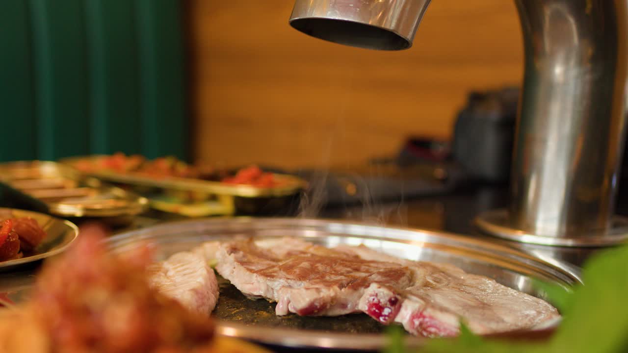 Raw meat slices cooking on tabletop grill, visible steam, warm lighting, shallow depth of field