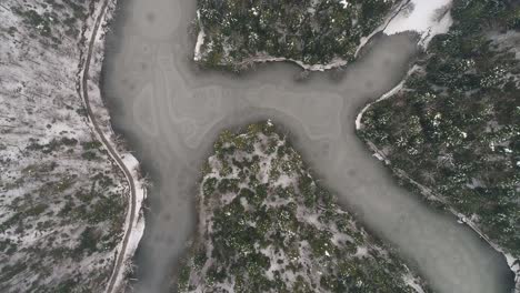 Aerial-shot-of-frozen-lake-surrounded-by-forest-at-winter