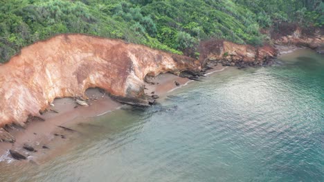 Aerial-cinematic-view-over-coastline-of-red-cliffs,-waves-and-ocean