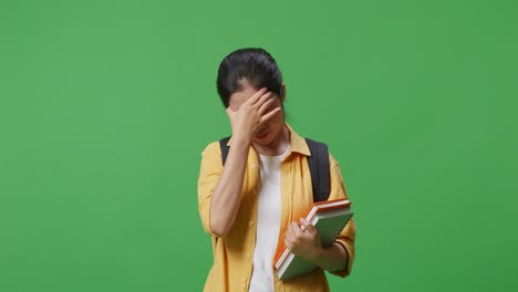 녹색 스크린 배경 스튜디오에 서 있는 동안 두통을 가진 배과 몇 권의 책을 가진 아시아 여성 학생