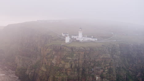 Toma-Aérea-De-Un-Faro-En-Lo-Alto-De-Un-Acantilado-En-Una-Mañana-Nublada-En-El-Norte-De-Escocia