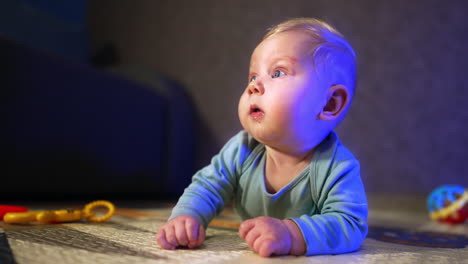 Cute blue-eyed Caucasian infant lies on his belly. Curious baby boy looking around him. Blurred backdrop.
