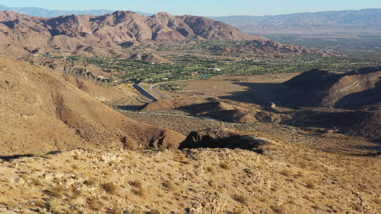 Ripresa drone che sorvola il bordo di una scogliera brulla, rivelando Palm Desert California in lontananza.