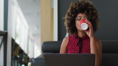 Mujer-De-Raza-Mixta-Pasando-Por-El-Papeleo-Tomando-Café-Usando-Una-Computadora-Portátil-En-La-Oficina