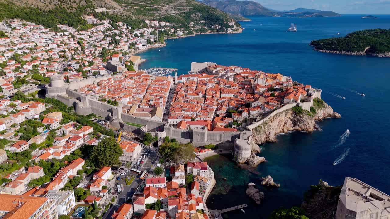 Wide aerial landscape drone captures Dubrovnik’s Old Town with terracotta rooftops, overlooking the deep blue Adriatic Sea, with rugged mountains rising in the background, bathed in soft, natural sun
