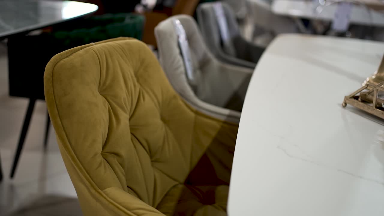 A unique yellow chair with a tufted design is positioned next to a sleek white table in a contemporary interior space. The surroundings complement the stylish decor, creating a cozy ambiance