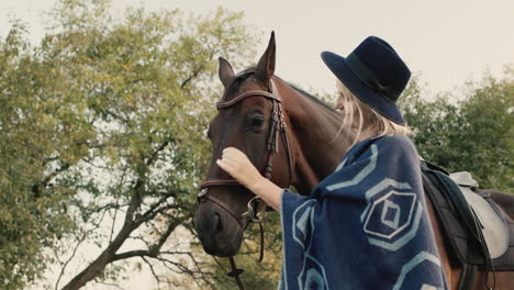 Portrait-of-a-stylish-woman-in-a-hat-and-poncho-near-a-horse-1