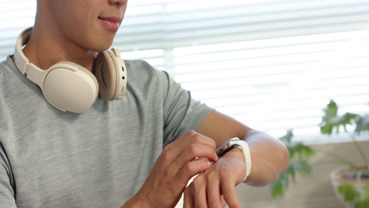Uomo asiatico che guarda lo smartwatch, toccando e scorrendo alla ricerca di un aggiornamento positivo vicino alle persiane