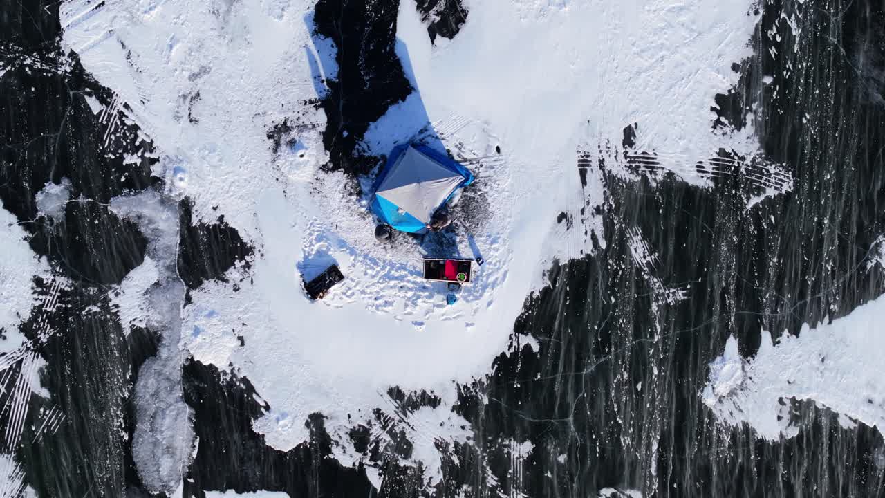Winter ice fishing with tents and snow blowing across Lake Geneva Wisconsin, slow motion aerial top shot static