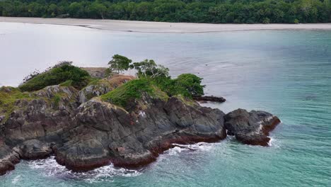 drone camera glides over a rocky, vegetated cape meeting turquoise waters, revealing dramatic coastline and lush greenery in soft daylight with smooth motion