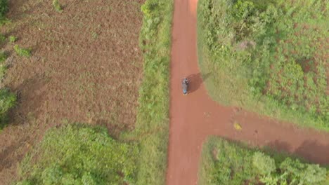 aerial birds eye view shot of a african man on a motorcycle riding on a dirt road through rural africa