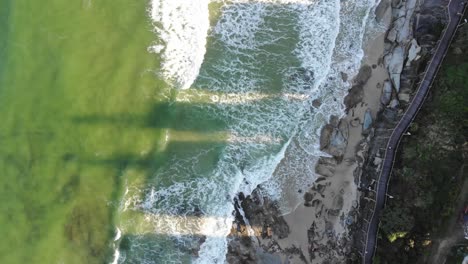 Volamos-Sobre-Un-Hermoso-Océano-Verde-Lima-Con-Toques-De-Azul-Que-Se-Encuentra-Con-Arena-Blanca-Pálida-Cortada-Por-Las-Sombras-Oscuras-Que-Se-Proyectan-Desde-Los-Edificios-De-Apartamentos-Que-Bloquean-La-Puesta-Del-Sol-De-La-Tarde