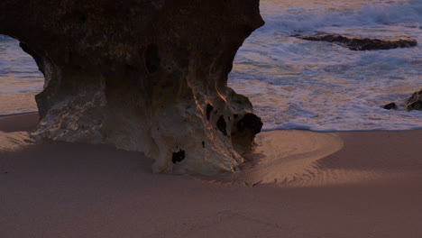 Waves-Splashing-On-Sandy-Shores-At-The-Beach-With-Rock-Formation-At-Sunset-In-Algarve,-Portugal