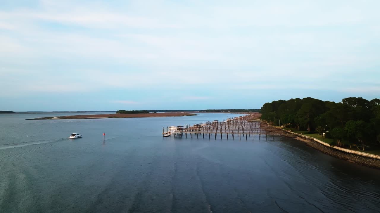 Colorful sunset fades behind boats moored by harbor town pier and calm shoreline, yacht drives to private dock, Harbour Town Pier South Carolina USA