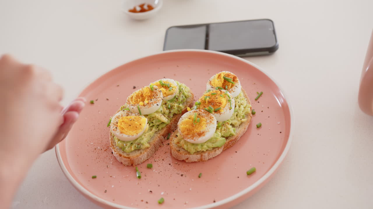 Preparing avocado toast with boiled eggs, asian woman reasoning breakfast on pink plate, at home