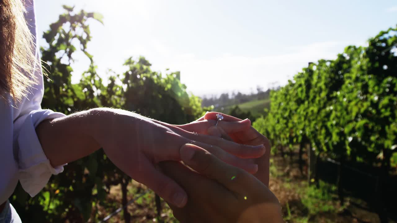 Uomo che mette l'anello di fidanzamento alla mano di una donna in vigneto
