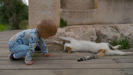 niño rubio repite la posición del gato acostado en tablas de madera