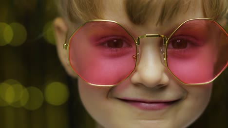 Close-up-face-of-child.-Smiling,-looking-at-camera.-Girl-in-pink-sunglasses-posing