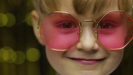 close up face of child. smiling, looking at camera. girl in pink sunglasses posing