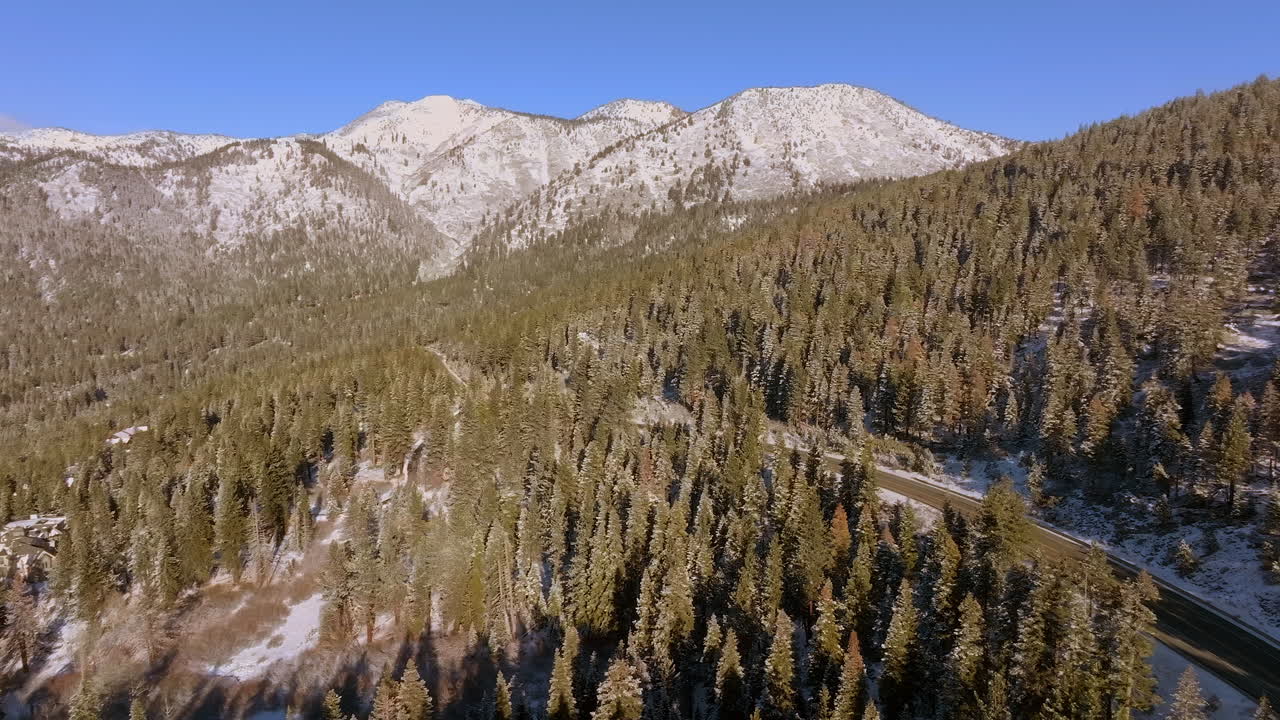 vista aérea panorámica del pico de la montaña y los abetos de douglas con un camino que serpentea y un automóvil que pasa por el lago tahoe, nevada en un hermoso día de invierno
