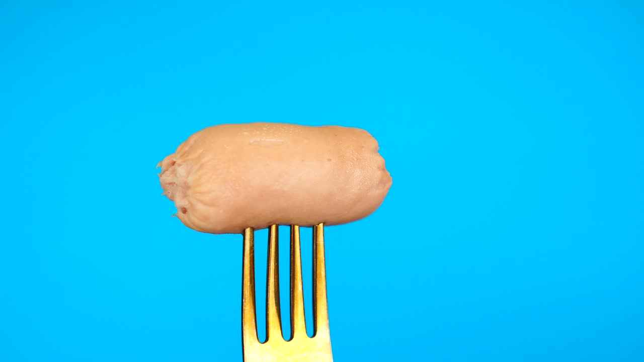 salchicha recién cocinada en el tenedor sobre fondo azul