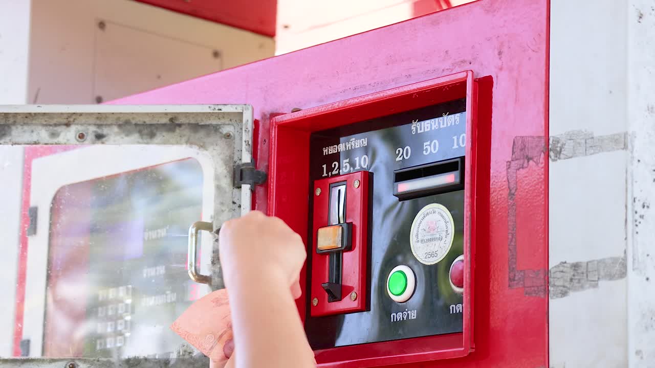 Una persona inserisce contanti in un distributore di carburante rosso a moneta in pieno giorno al punto panoramico di Khao Rang, Phuket.