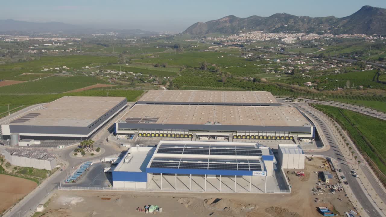 Centro di distribuzione e magazzini industriali con montagne e un villaggio sullo sfondo
