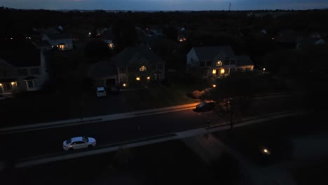 aerial flight over dark american housing area with street and lighting window of house. drone landing shot. parking cars on street. dusk scene in suburbia.