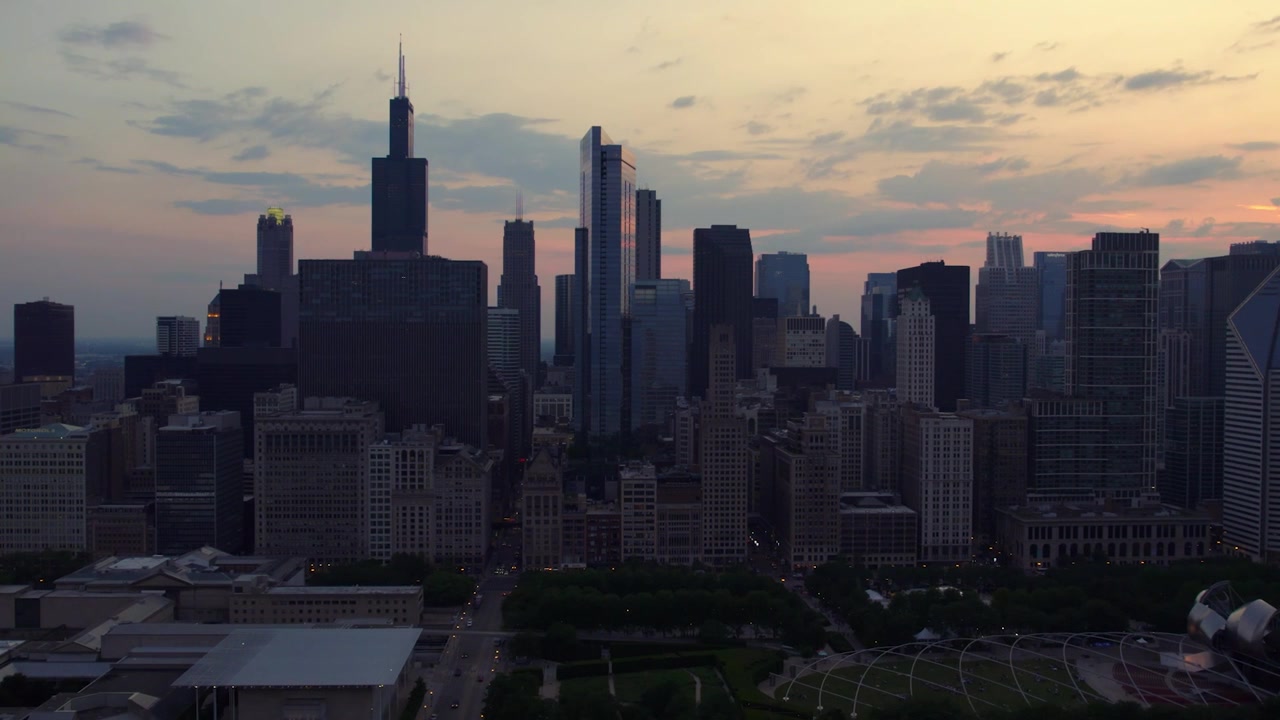 Vista aérea ampla de drone do centro de Chicago, apresentando a Willis Tower, Millennium Park, arranha-céus densos e um céu colorido ao pôr do sol.