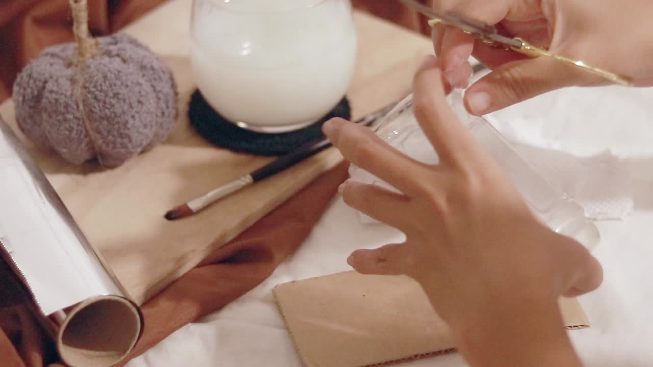 Hands using scissors in cutting plastic bottle in a recycling craft project on a table with a cozy autumnal mood setup