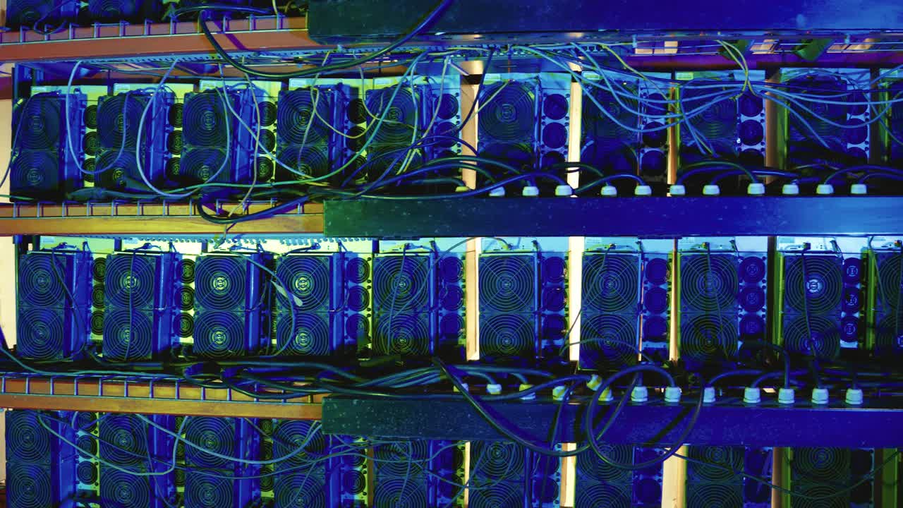 Stacked shelves of bitcoin mining machines with fans and tangled wires with visible cooling fans and tangled wiring on metal shelves in a server room. Side view, pan right