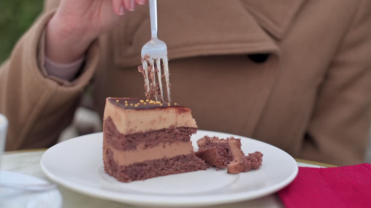 Woman in brown coat eating chocolate cake with coffee at a terrace