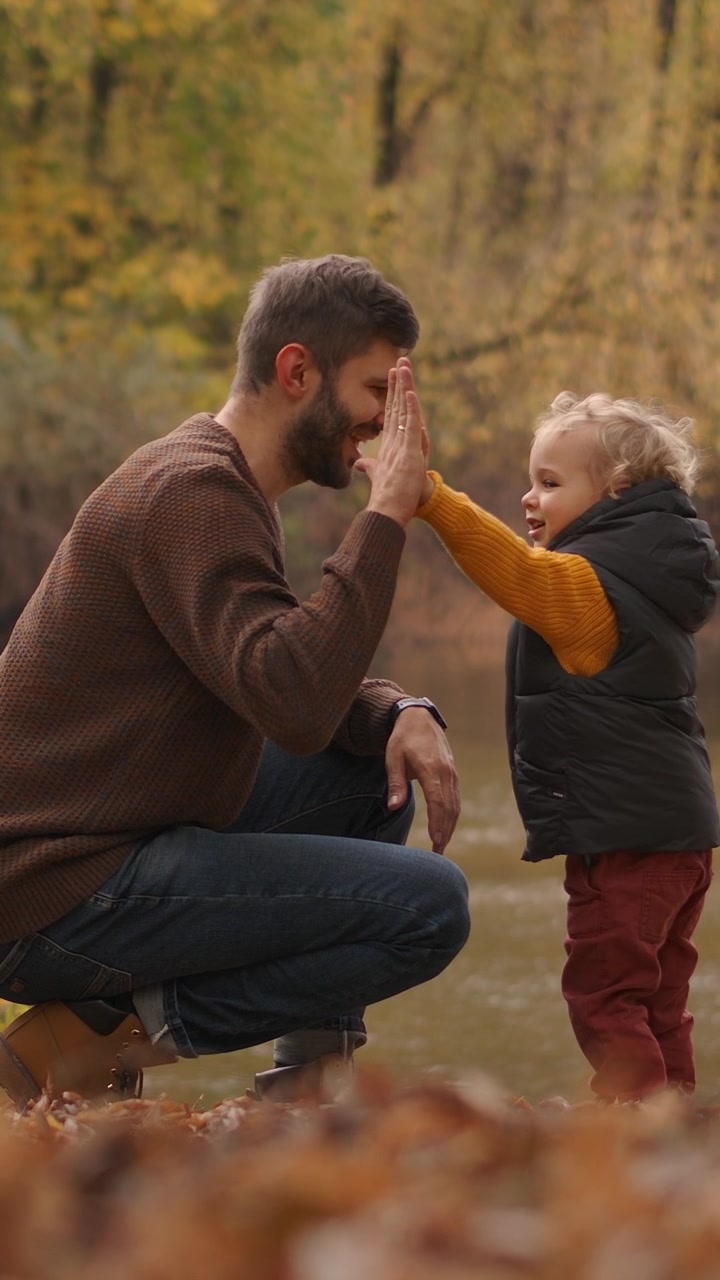 Padre e figlio piccolo che si danno il cinque vicino al fiume in autunno