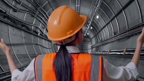 close up back view of a female engineer with safety helmet spreading arms in underground subway tunnel