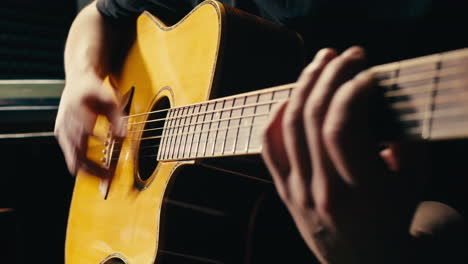 young musican man checking strings of acoustic guitar close-up. male guitarist tuning sound of musical instrument.