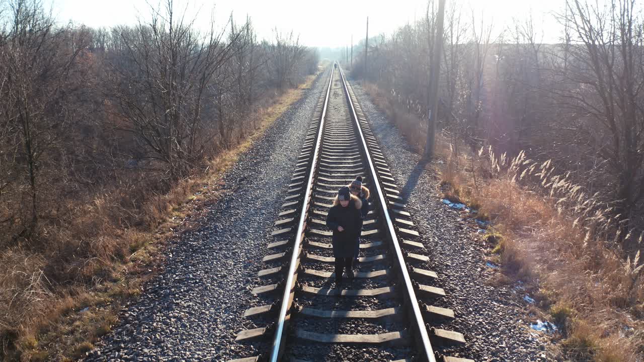 Two little boys walking on a railroad. Children in warm clothes go on a rail on nature background in winter time.