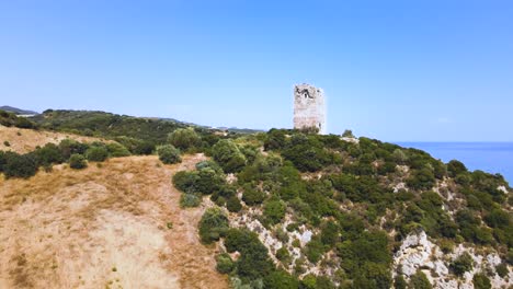 Upwards-moving-aerial-drone-clip-over-a-sandy-beach-towards-an-ancient-tower-in-Kavala,-Macedonia,-Greece