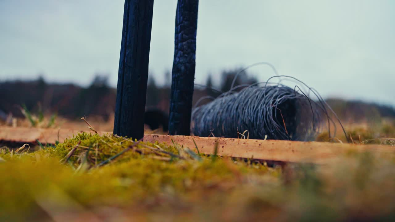 A Coil of Wire Was Tossed Near a Blackened Wooden Pole Standing Upright on the Ground - Defocused Shot