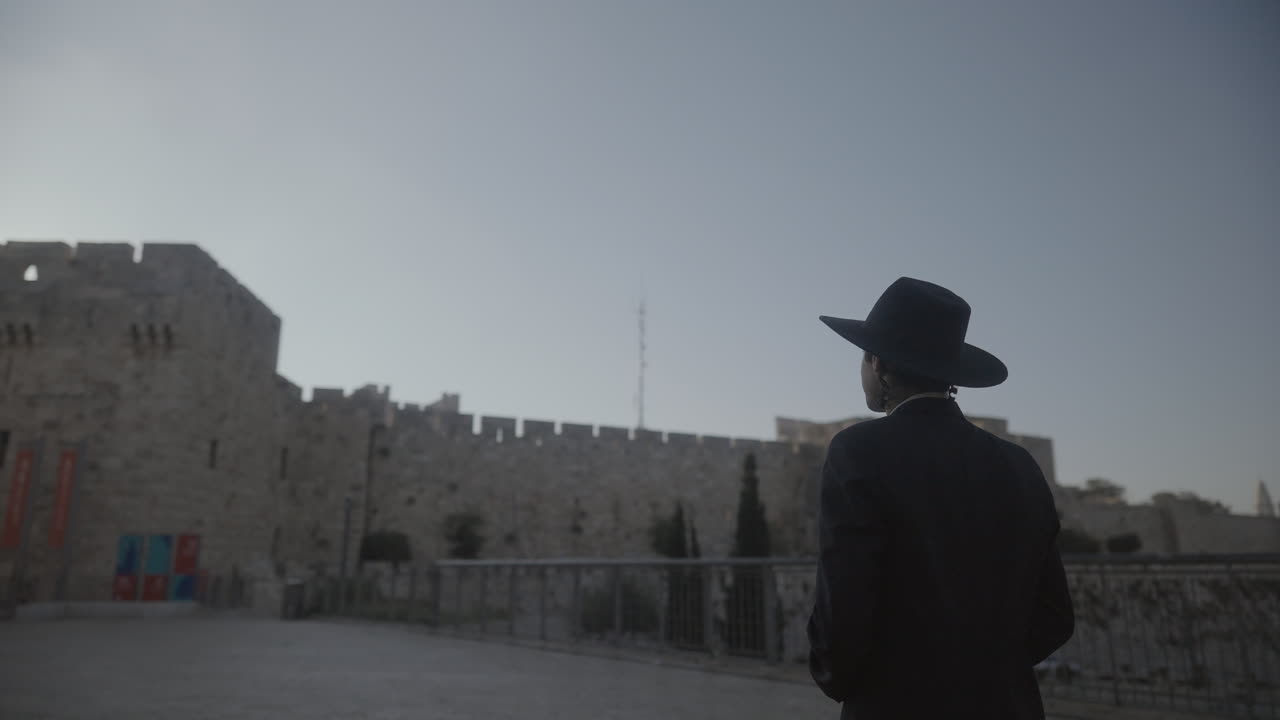 Panoramica di un uomo in abito nero e cappello che esplora un vecchio castello a Gerusalemme