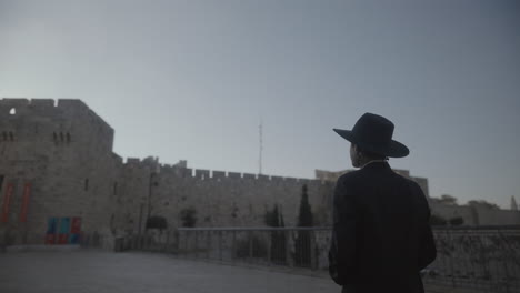 pan view of a man in black suit and hat exploring an old castle in jerusalem