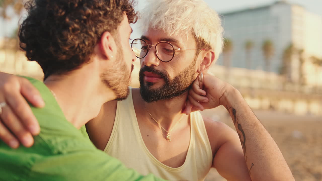 仲睦まじいゲイカップルが晴れたビーチで抱き合いキスをする